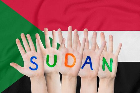 Inscription Sudan on the children's hands against the background of a waving flag of the Sudanの写真素材