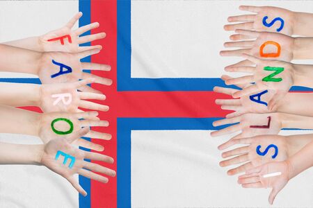 Inscription Faroe Islands on the children's hands against the background of a waving flag of the Faroe Islandsの写真素材
