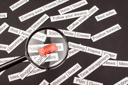 Magnifier glass over the red inscription Goals cut out of paper. Surrounded by other inscriptions on a dark background. Word cloud concept.の写真素材
