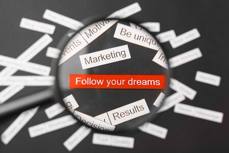 Magnifier glass over the red inscription follow your dreams cut out of paper. Surrounded by other...