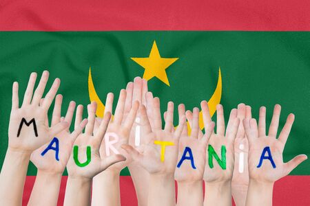 Inscription Mauritania on the children's hands against the background of a waving flag of the Mauritaniaの写真素材