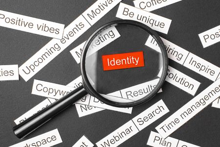 Magnifier glass over the red inscription identity cut out of paper. Surrounded by other inscriptions on a dark background. Word cloud concept.の写真素材