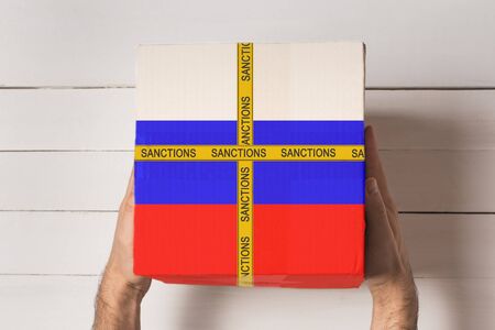 Yellow tape with the inscription Sanctions on the box with the flag of Russia in male hands. Top...