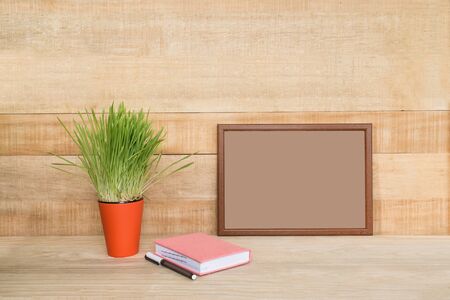 Empty frame on a wooden wall. Notebook and pen, green houseplant on the table. Working space at home