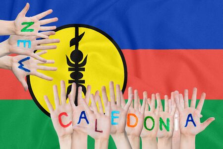 Inscription New Caledonia on the children's hands against the background of a waving flag of the New Caledoniaの写真素材