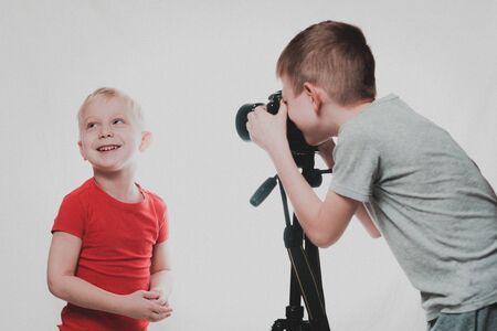 Boys are photographing each other with a SLR camera. Home studio. Young blogger. White background
