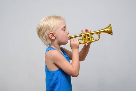 Little cute blond boy playing trumpet on light background.の写真素材