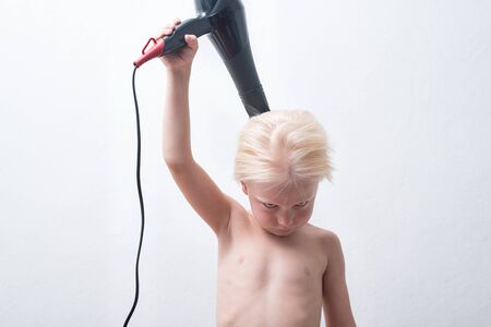 Serious blond boy with wet hair is blow dry. White backgroundの写真素材