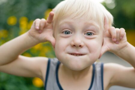 Funny blond boy makes faces. Preschooler. Sunny dayの写真素材