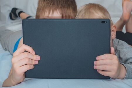 Two boys are lying in bed and looking at the tablet. Leisure gadgetsの写真素材