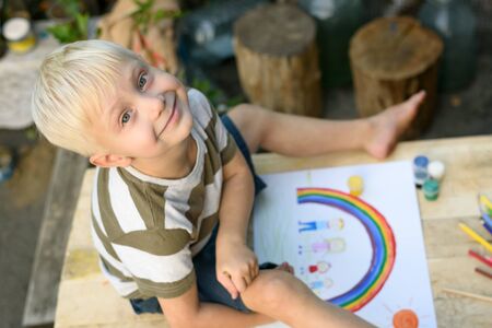Cute boy draws rainbow and family. Open air. Top view. Creative concept.の写真素材