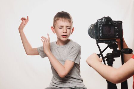 Boy enthusiastically sings in front of the camera. Children's hands with a camera in the frame. Young video blogger. White backgroundの写真素材