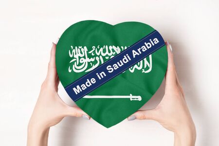 Inscription Made in Saudi Arabia the flag of Saudi Arabia. Female hands holding a heart shaped box. White background.の写真素材