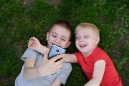 Two boys make selfie on a smartphone while lying on the grass. Top viewの写真素材