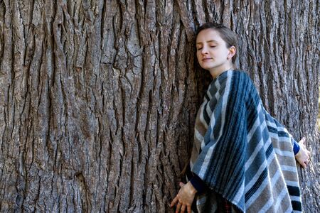 Young woman leaning against the trunk of a large tree. Closed eyes. Unity with natureの写真素材