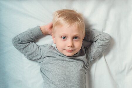 Blond cute boy lies hands behind his head. White backgroundの写真素材