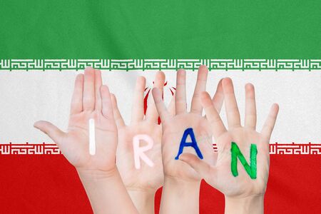 Inscription Iran on the children's hands against the background of a waving flag of the Iranの写真素材