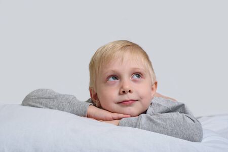 Blond boy lies with his head in his hands and looks up. White backgroundの写真素材