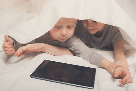 Two boys lying and watching something on a tablet, hid under the covers. Gadget Leisureの写真素材