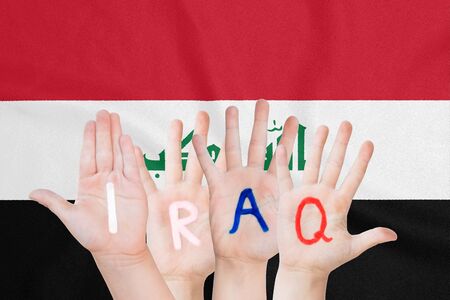 Inscription Iraq on the children's hands against the background of a waving flag of the Iraqの写真素材