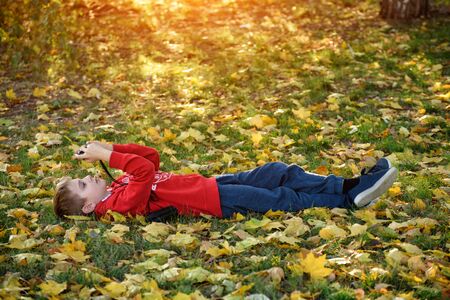 Boy takes pictures while lying on his back. Lawn with autumn foliage. sunny dayの写真素材