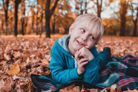 Cute little blond boy lies on a plaid, yellow autumn leaves. Smiling and having fun. Fall dayの写真素材