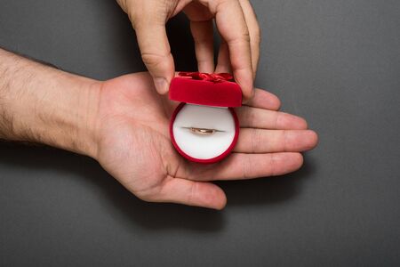 Open red jewelry box with ring in a male hands. Present. Black background
