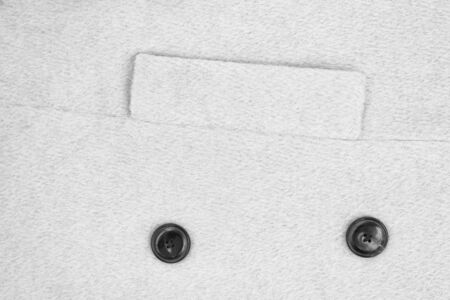 White textured woolen coat fabric with a lapel pocket and two buttons. Close-upの写真素材