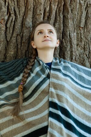 Young woman leaned her back against the trunk of a large tree. Unity with nature