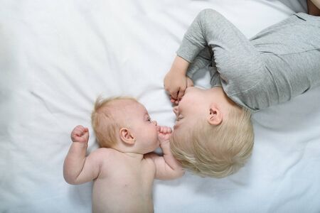Baby and smiling older brother are lying on the bed. Funny and interact. Top viewの写真素材
