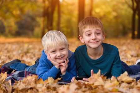 Two little brothers lying in yellow autumn leaves. Smiling and having fun. Fall dayの写真素材