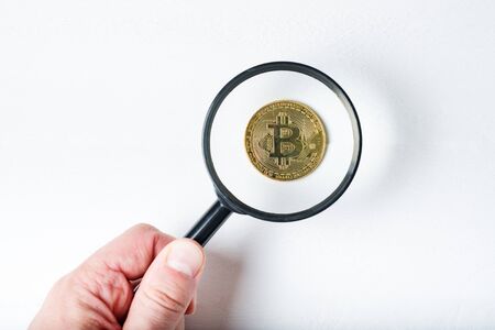 Bitcoin coin through a magnifying glass in a male hand