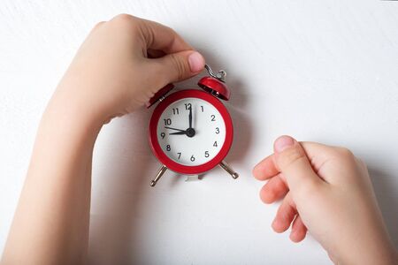 Red alarm clock in children's hands on a white background.の写真素材