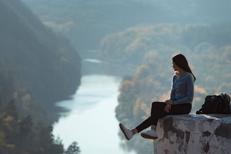 Girl sitting on the hill and looks into the distance of the forest and the river.