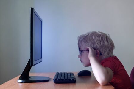 Blond boy with glasses sits his nose buried in a monitor. Internet and preschoolerの写真素材
