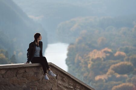 Girl sitting on the hill and looks into the distance of the forest and the river.の写真素材