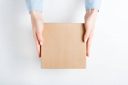 Square cardboard box in female hands. Top view, white background