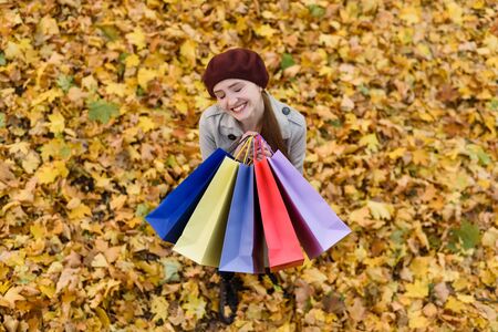 Smiling happy young woman shopaholic with colorful bags. Autumn leaves on background