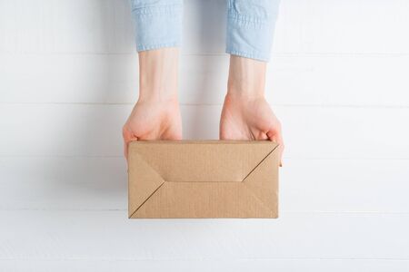 Rectangular cardboard box in female hands. Top view, white background