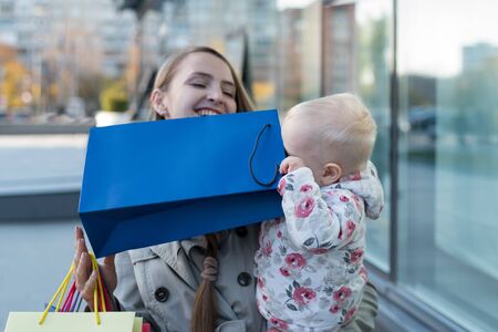 Happy young mother with a little daughter in her arms and having fun with bags. Shopping day. Mall on the backgroundの写真素材