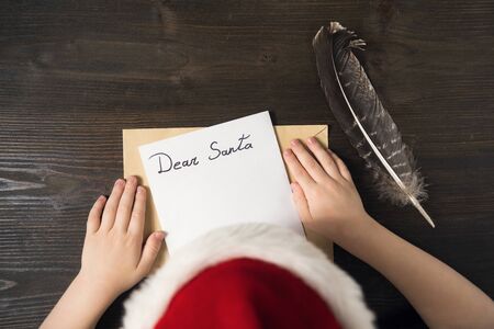 Child in Santa hat writing a letter to Santa. Wooden backgroundの写真素材