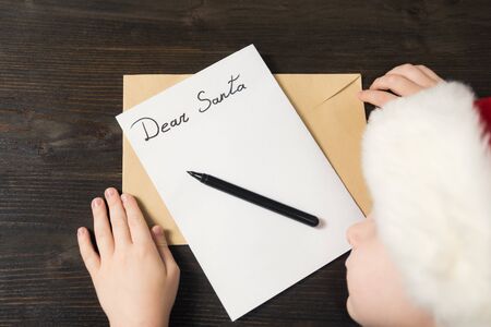 Child in Santa hat is sleeping at the table. Letter for Santa. Wooden background.の写真素材