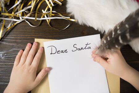 Child hand writes letter to Santa. Tinsel, wooden background.の写真素材