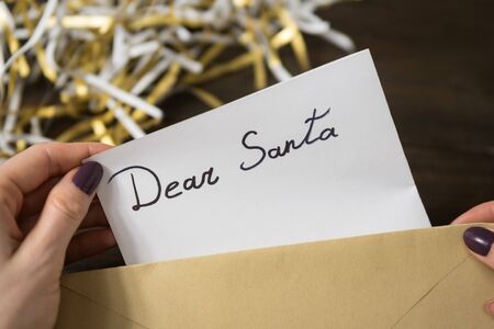Female hands put a letter for Santa in an envelope. Wooden background. Close-upの写真素材