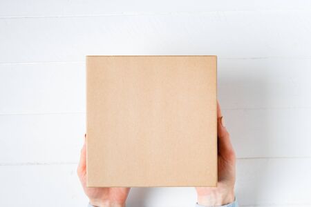 Square cardboard box in female hands. Top view, white backgroundの写真素材