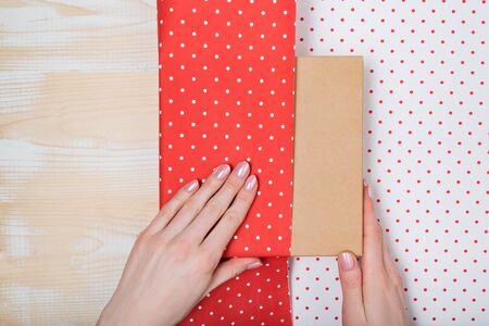 Female hands pack a gift in white-red polka-dot paper. Top viewの写真素材