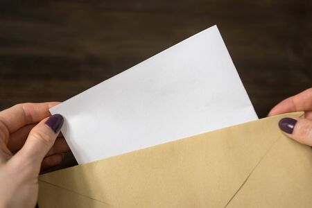 Female hands put a letter in an envelope. Wooden background. Close-up
