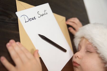 Child in Santa hat is sleeping at the table. Letter for Santa. Wooden background.の写真素材