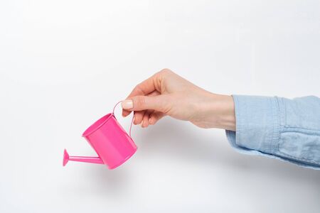 Small pink watering can in a female hand on a light background.の写真素材