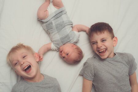 Two older brothers and youngest baby in a white bed. Happy childhood, big family. Top viewの写真素材